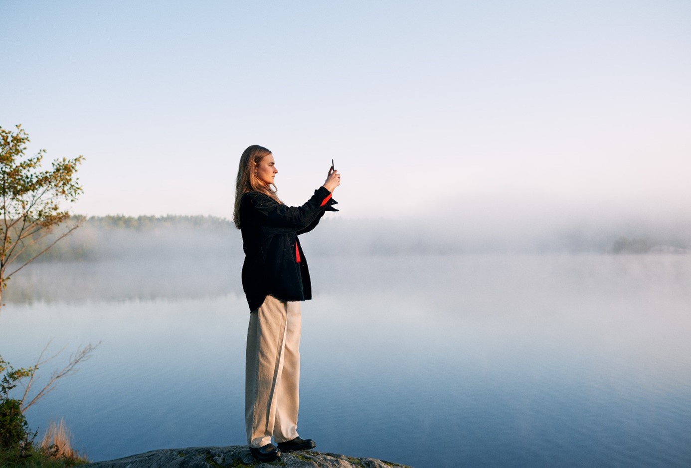 En person som står på en klippa och fotograferar med en smartphone.