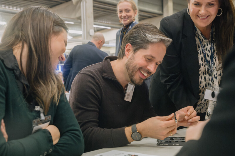Three people are smiling while repairing a mobile phone.